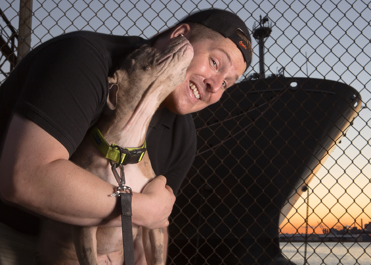 Photo of professional pet photographer, J.B. Shepard, in front of the Baltimore Inner Harbor, seen posing with a pit bull rescue dog from a local foster group.