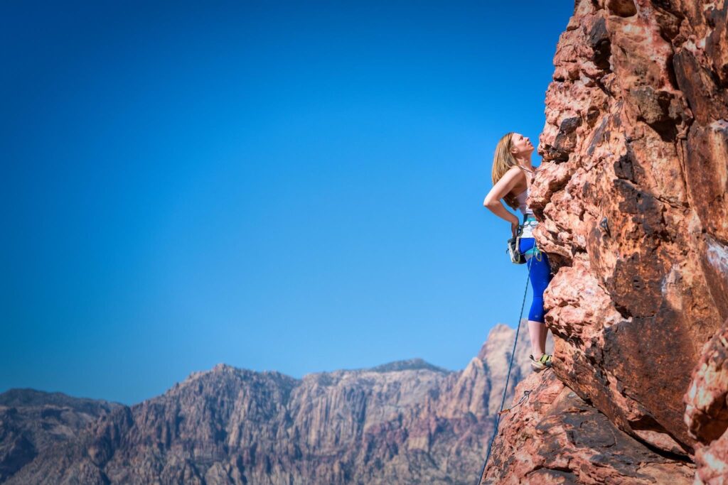 A photo of Jennifer Morrison, founder of DogVenture Gear and rock climbing enthusiast, climbing a cliff face in Arizona. 